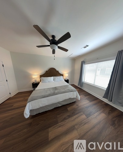 A bedroom with a bed, a ceiling fan, and a window with curtains.