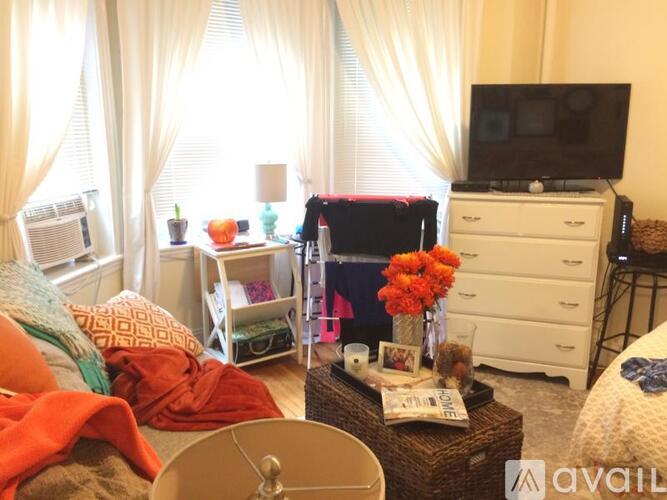 A messy bedroom with a bed, dresser, and window with curtains.