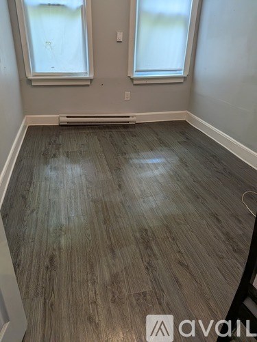 A room with wooden flooring and two windows.