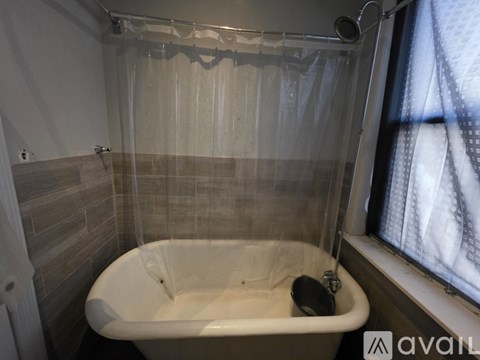 A white bathtub with a shower curtain and a window with curtains.