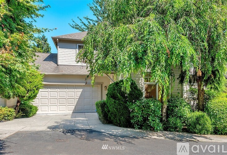 A house with a white garage door is surrounded by greenery.