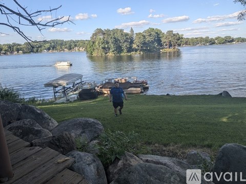A person is walking on a grassy area near a lake with a dock and a boat.