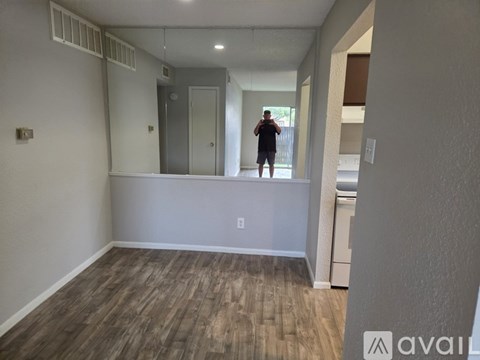 A man is standing in a room with wooden flooring and white walls.