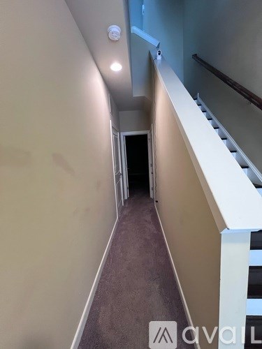 A hallway with a carpeted floor and a white railing on the right side.
