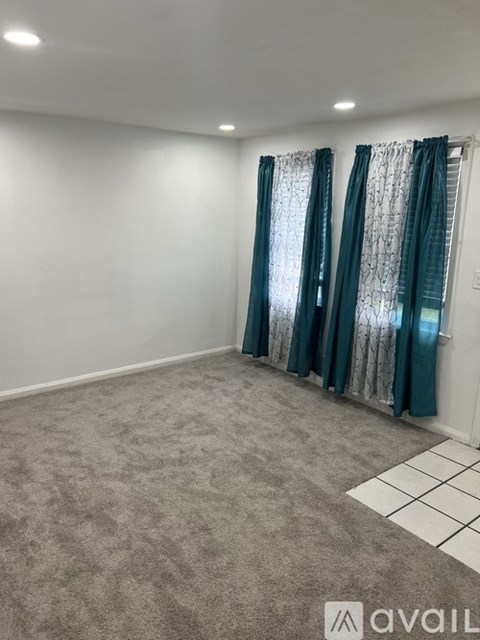 A room with grey carpet and a window with curtains.