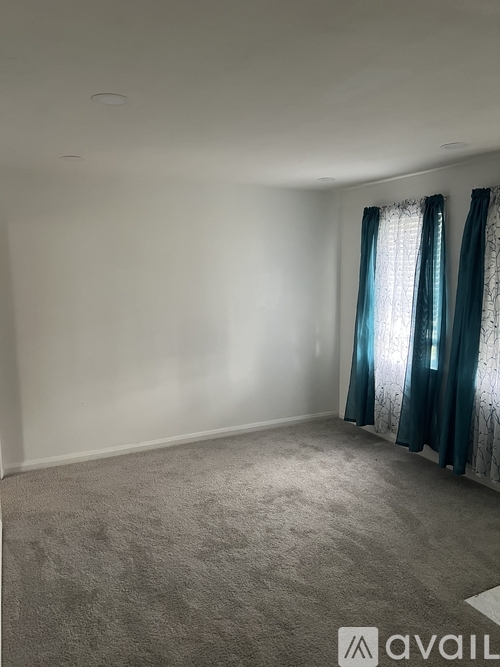 A room with a carpeted floor and a window with curtains.