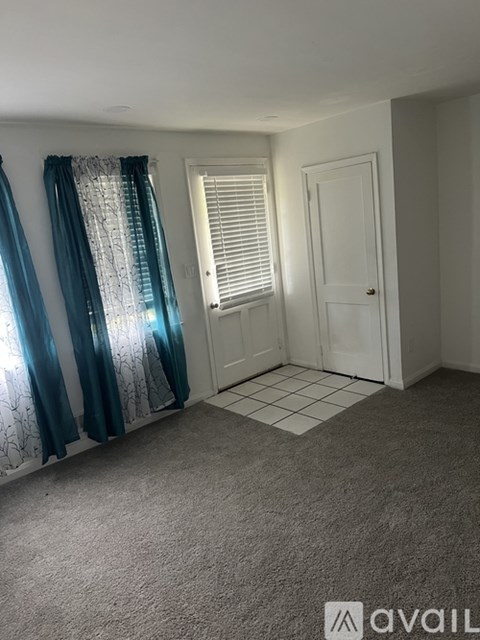 A room with a carpeted floor and a window with curtains.