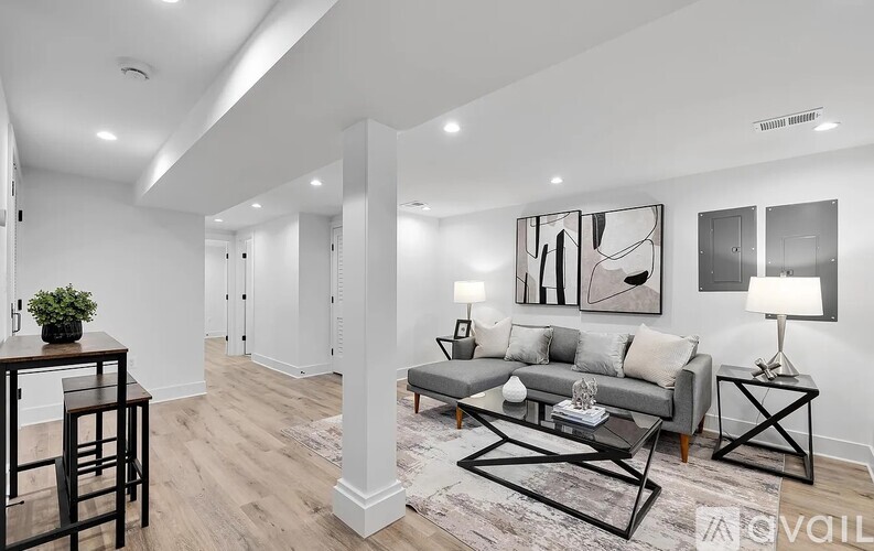 A modern living room with a grey sofa, a black coffee table, and a painting on the wall.