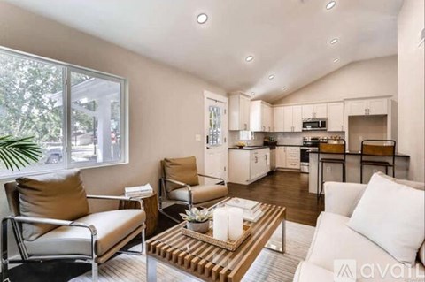 A living room with a couch, chairs, and a coffee table in front of a kitchen.