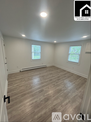 A room with wooden flooring and two windows.