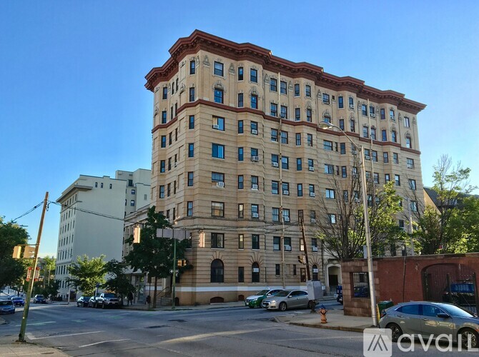 A large, beige building with a red roof is situated on a street corner with cars parked in front.