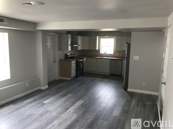 A spacious kitchen and living room with wood flooring and white walls.