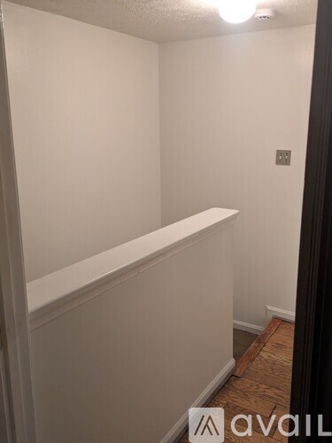 A white wall with a light switch and a wooden floor.