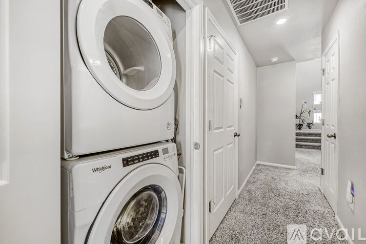 A white Whirlpool washing machine and dryer in a small, carpeted laundry room.