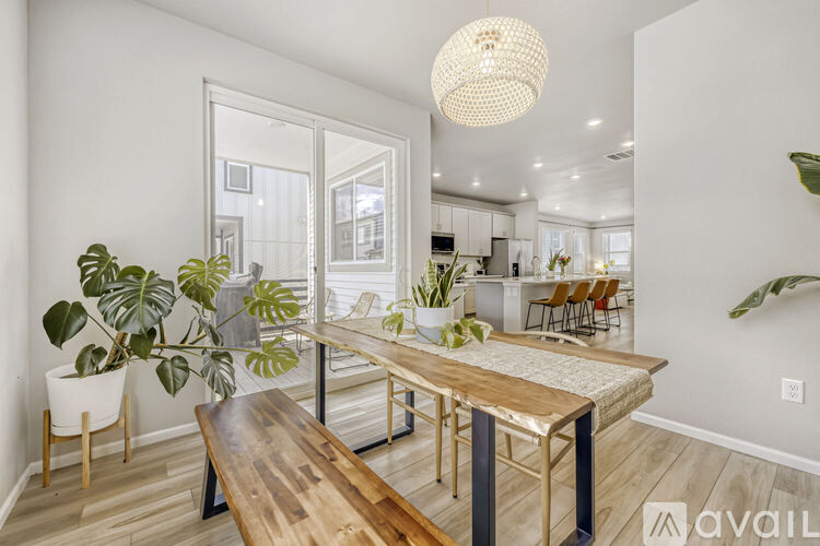 A modern dining room with a wooden table and bench, a potted plant, and a hanging light fixture.