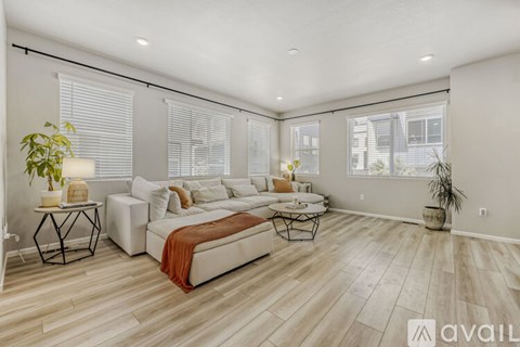 A spacious living room with a white sofa set and wooden flooring.