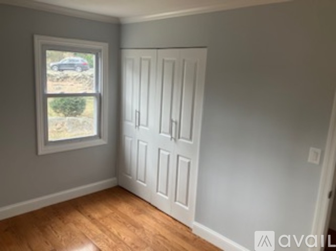 A room with a white door and a window showing a car and trees outside.