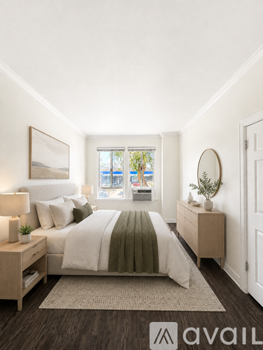 A bedroom with a large bed, a nightstand, and a window overlooking the city.
