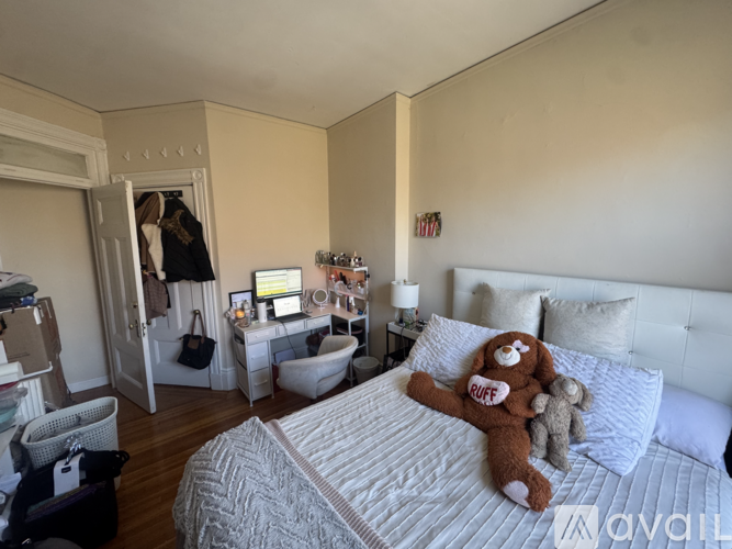 A bedroom with a bed, a chair, a desk with a computer, a couch, a wardrobe, and a nightstand with a lamp.