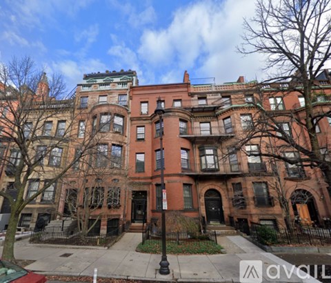 A row of brown brick townhouses with black iron fences and bare trees in front.