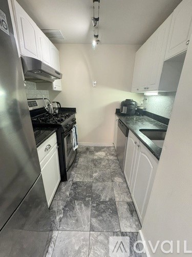 A kitchen with a stainless steel refrigerator and black countertops.