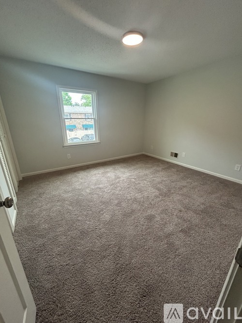 A room with a carpeted floor and a window showing trees and a building outside.