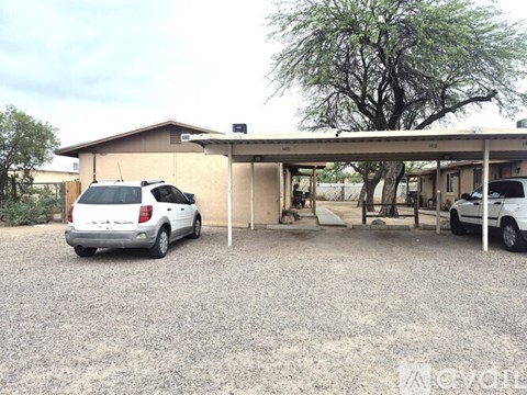 A white car is parked in a gravel lot in front of a building.