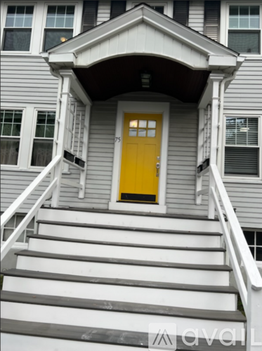 A grey house with a yellow door and white stairs.