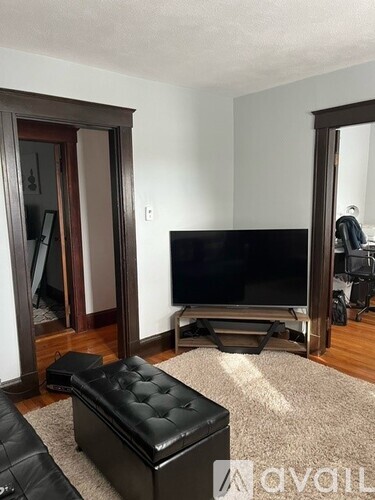 A black leather ottoman sits in front of a flat screen TV in a living room.