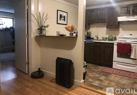 A black speaker stands on a wooden floor in a kitchen.