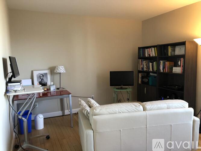 A living room with a white couch, a television, a desk with a lamp, and a bookshelf.