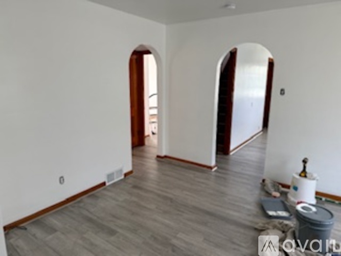 A room with wooden floors and white walls with two arched doorways.