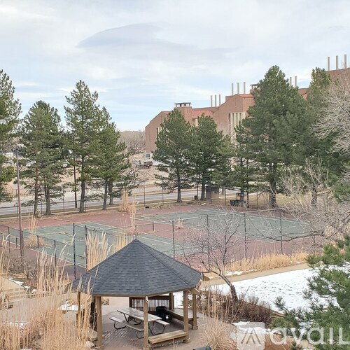 A gazebo sits in front of a tennis court with snow on the ground.