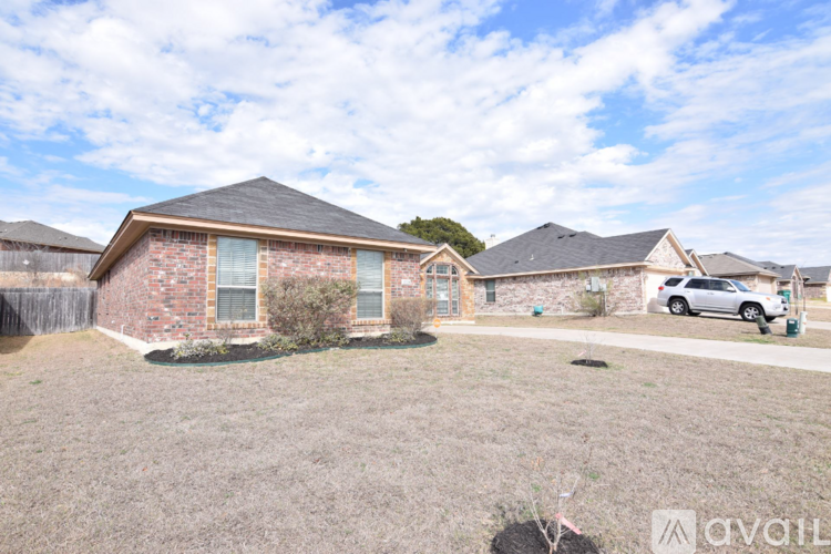 A house with a brown brick exterior and a grey roof is surrounded by a grassy area and other houses in the background.
