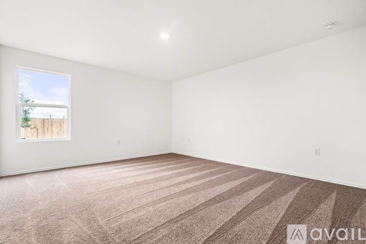 Empty room with carpeted floor and a window showing a fence and trees outside.