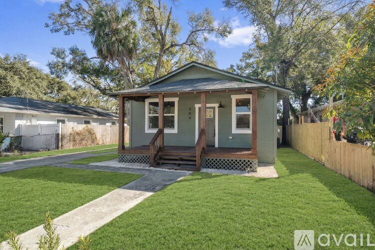 A small house with a porch is surrounded by a green lawn and trees.