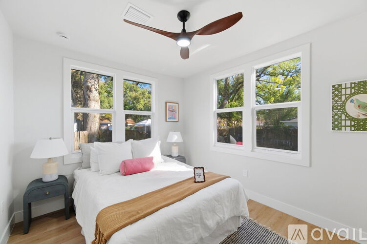 A bedroom with a bed, a ceiling fan, and a window with a view of trees.