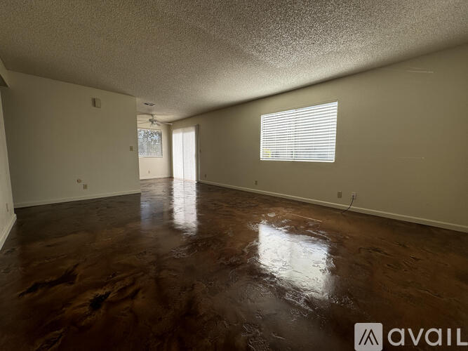 A room with brown flooring and a window with blinds.