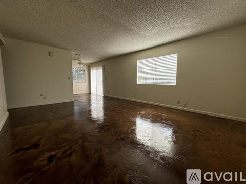 A room with brown flooring and a window with blinds.