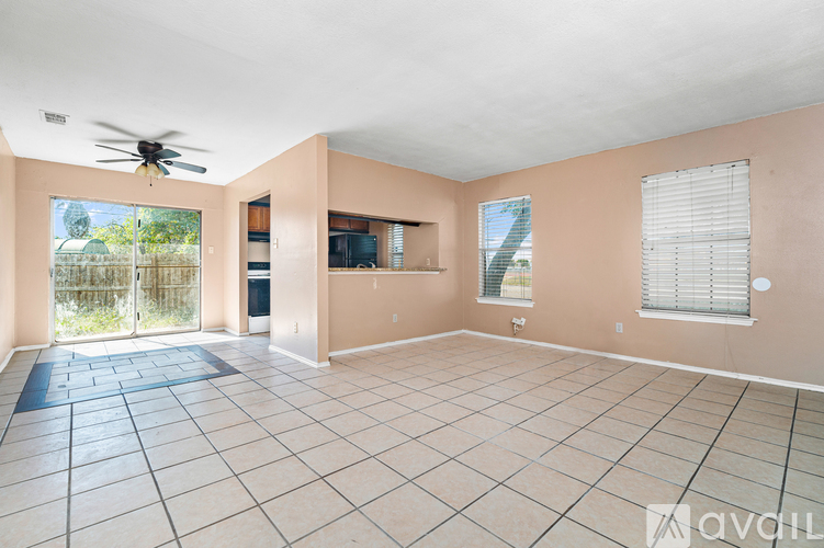 A spacious room with a ceiling fan and sliding glass doors leading to a backyard.