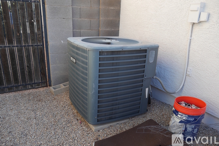 A gray air conditioner unit is placed on a gravel surface outside a building.
