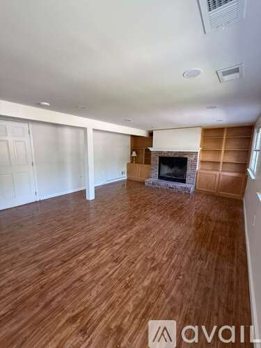 A spacious room with wooden flooring and a fireplace.