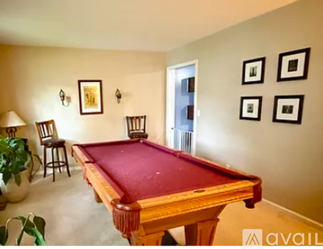 A pool table is in the middle of a room with a plant and chairs.