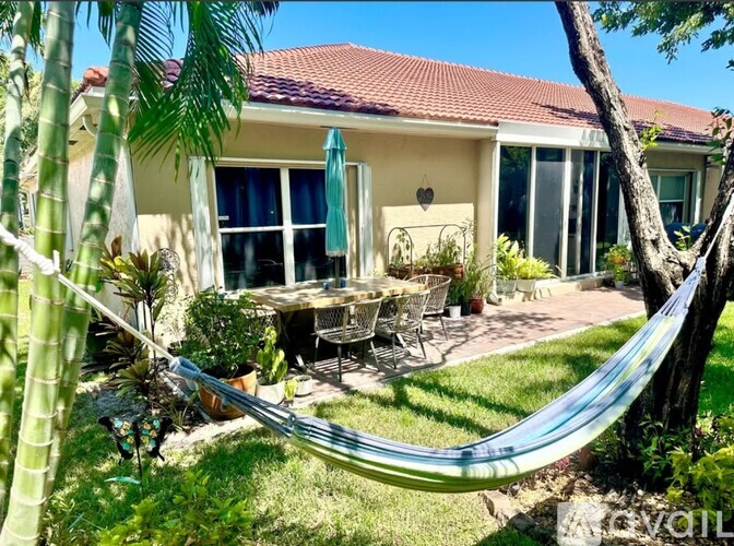 A hammock is strung between two trees in a backyard.