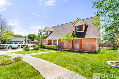 A house with a red door and a brown roof is surrounded by a grassy lawn and a sidewalk.