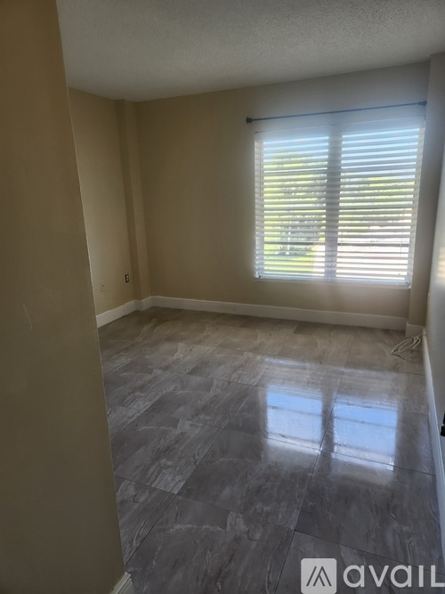 A room with a window covered by blinds and a grey floor.