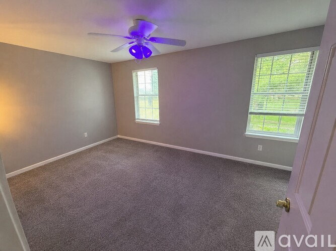 A room with a ceiling fan and two windows.