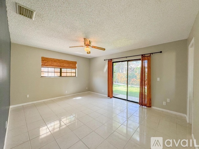 A spacious room with a ceiling fan and sliding glass doors leading to a garden.