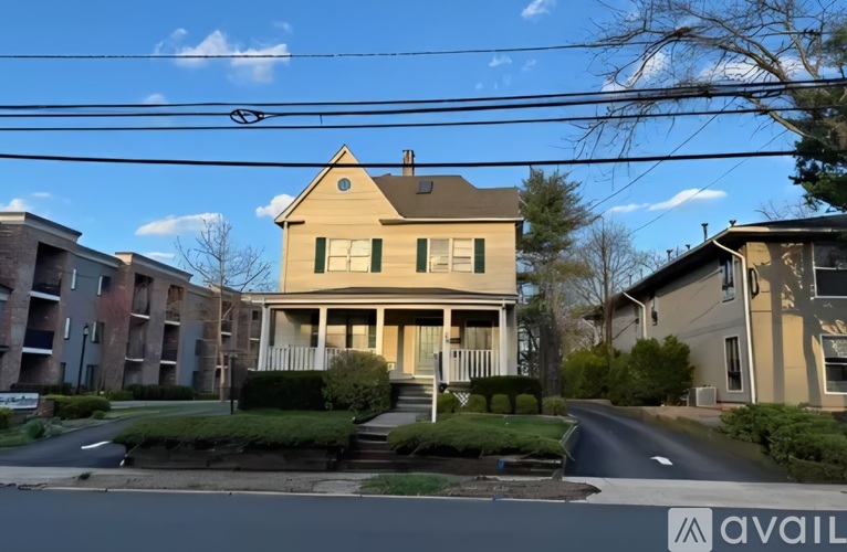 A house with a porch and a front yard is in front of apartment buildings.