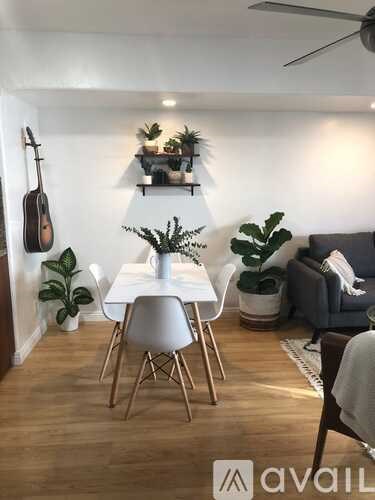 A living room with a white dining table and chairs, a guitar hanging on the wall, and a couch with a blanket on it.